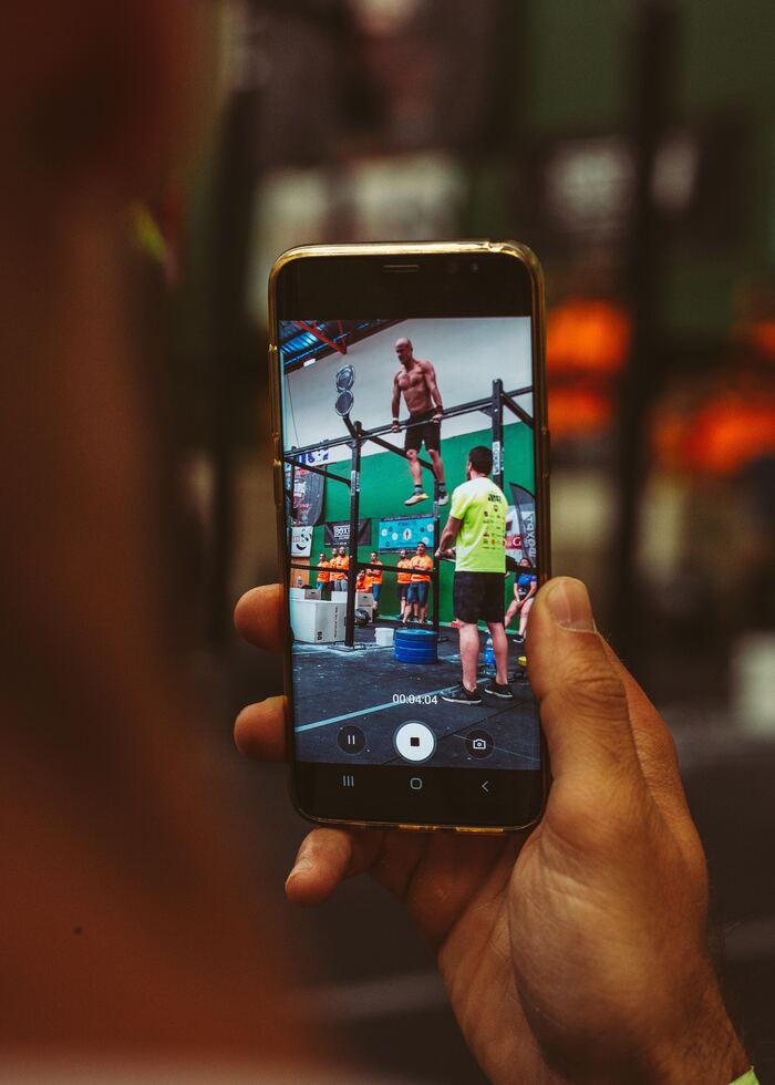 Mano sujetando un móvil que graba a un atleta en pleno workout